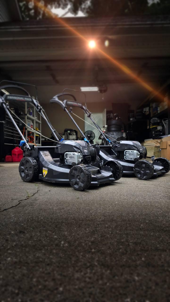 Two Personal Pace push mowers outside a garage